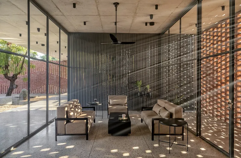 Interior living space with concrete ceiling and corrugated metal screen filtering dappled light from the courtyard