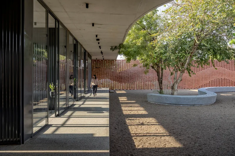 Covered walkway with vertical metal fins casting striped shadows onto the concrete floor and courtyard beyond