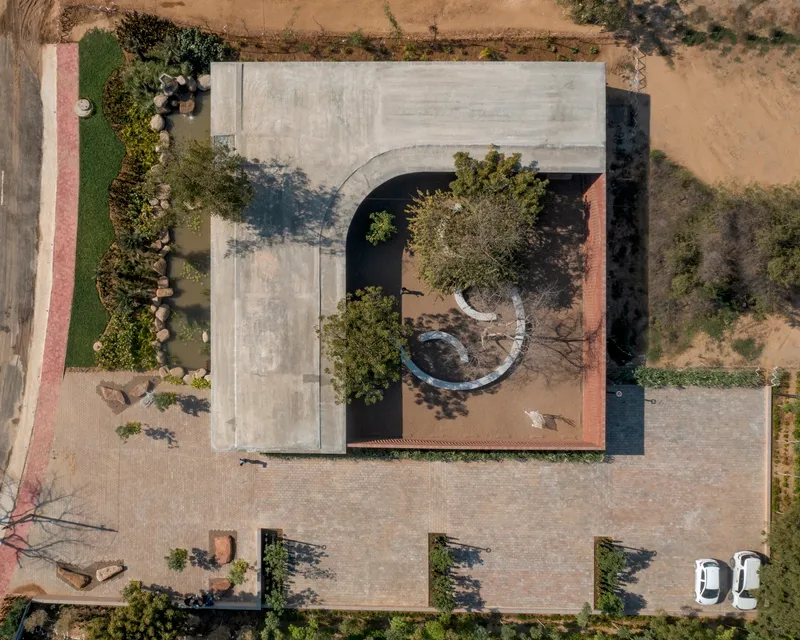 Drone view of the curved concrete roof cutout revealing the courtyard tree and circular bench below