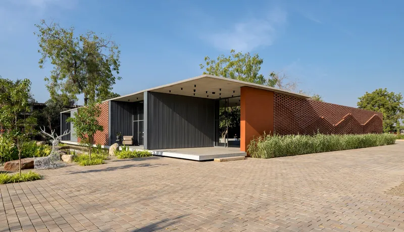 Street view of the low-slung pavilion with zigzagging perforated brick wall and planted beds