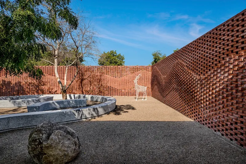 Enclosed courtyard with perforated brick walls surrounding a curved concrete planter and gravel floor