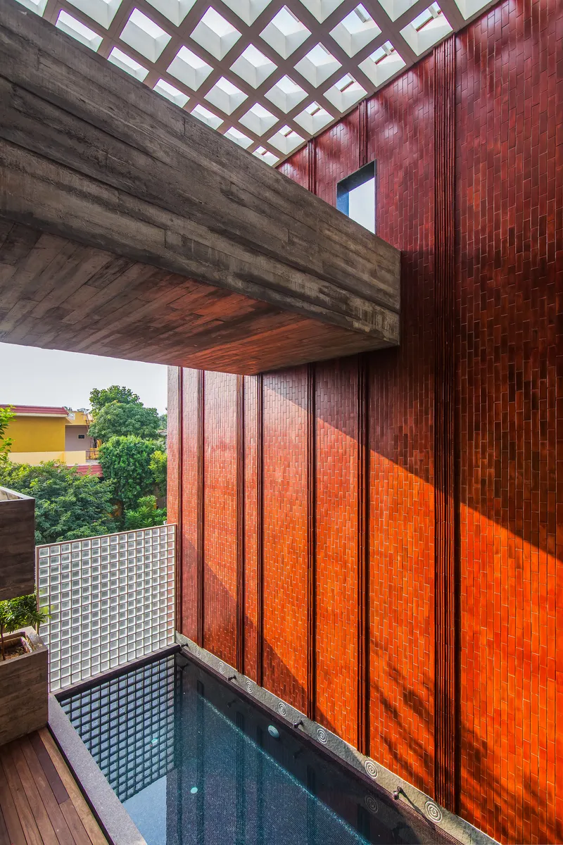 Cantilevered concrete balcony above a courtyard pool with red terracotta tile wall and gridded skylight