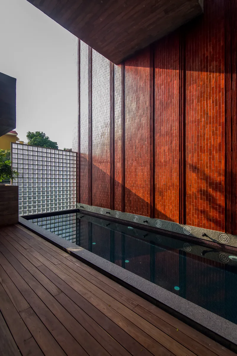 Terrace pool edged with timber decking adjacent to terracotta tile wall and glass block screen
