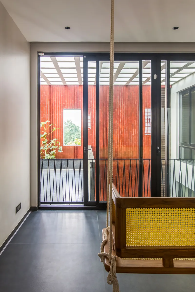 Interior corridor with rope swing and glazed doors opening to terracotta-clad courtyard under pergola