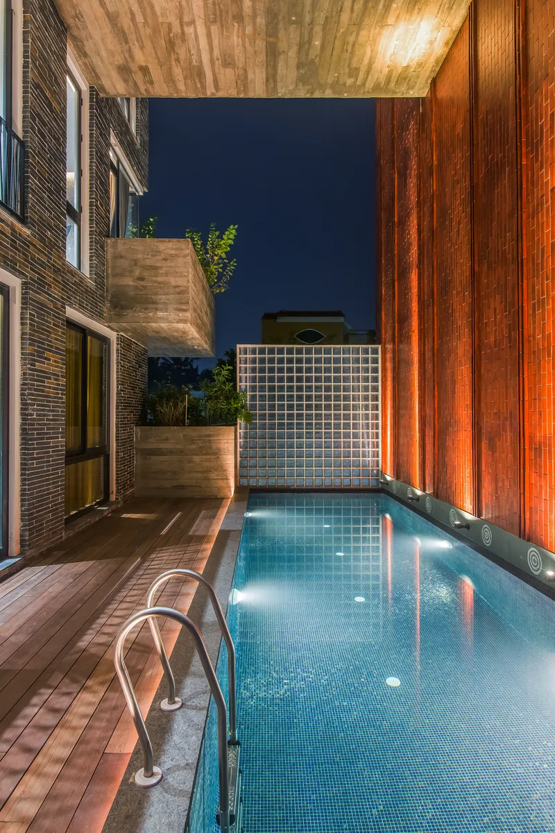 Courtyard pool flanked by timber decking and cantilevered concrete planters at twilight