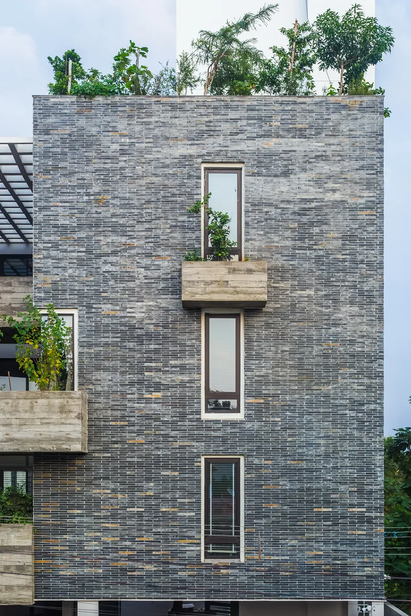 Street facade in variegated grey brick with three cantilevered concrete planters and rooftop greenery