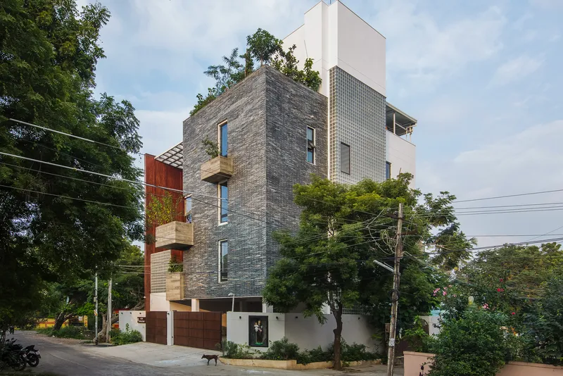 Street view of the stacked facade with grey brick, white block panels, and cantilevered timber balconies