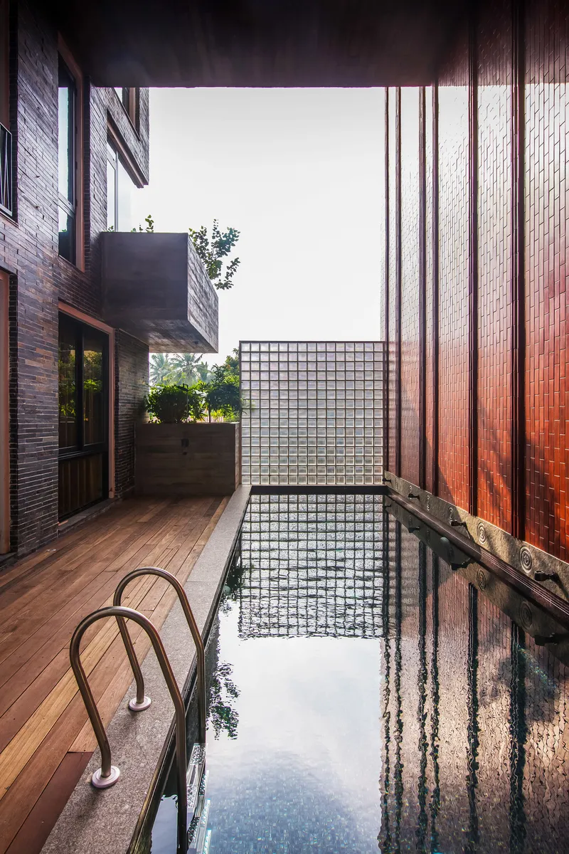 Narrow courtyard pool with timber deck and glass block wall under an open sky