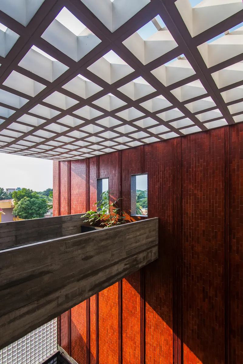 Interior bridge with concrete planters beneath a diagonal timber grid ceiling and woven tile walls