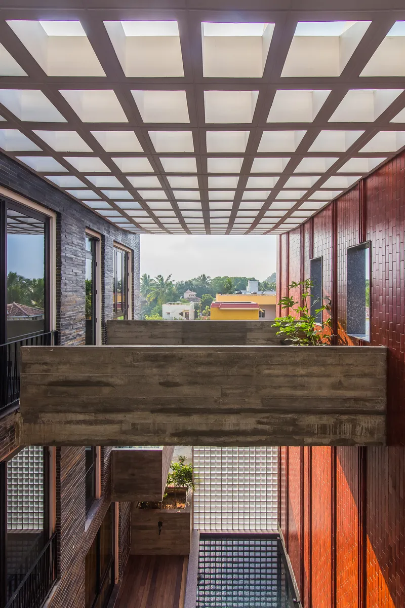 Double-height interior courtyard with gridded skylight above a concrete bridge and planted terrace