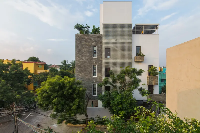 Street facade combining stacked stone, glass block panels, and white stucco volumes with planted balconies