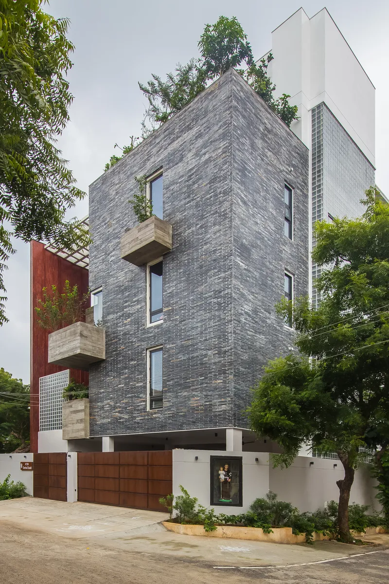 Corner view of the grey brick tower with projecting balconies and surrounding trees under overcast sky