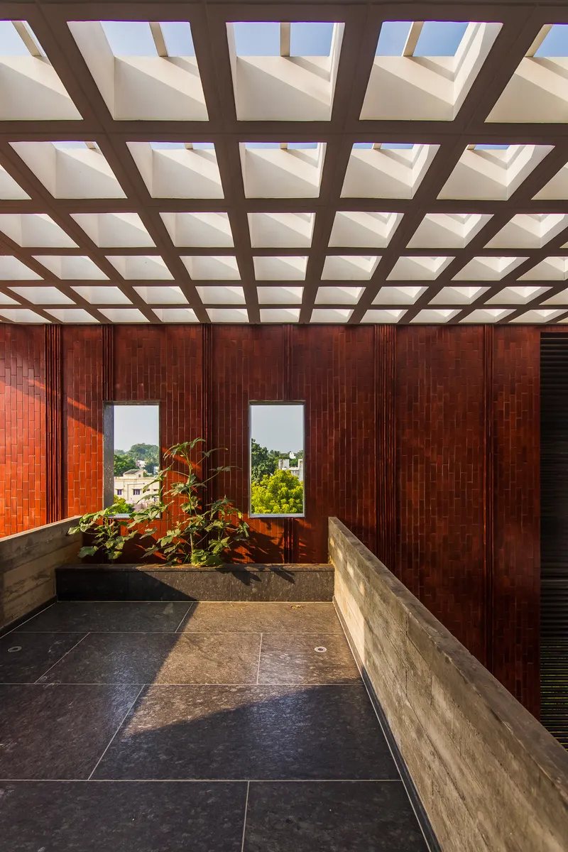 Upper terrace enclosed by vertical timber slats under a coffered skylight grid with planted bed