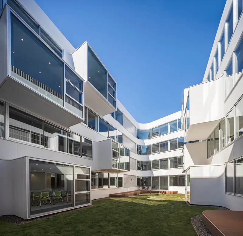 Internal courtyard with planted lawn surrounded by white facades and continuous balconies under a clear sky