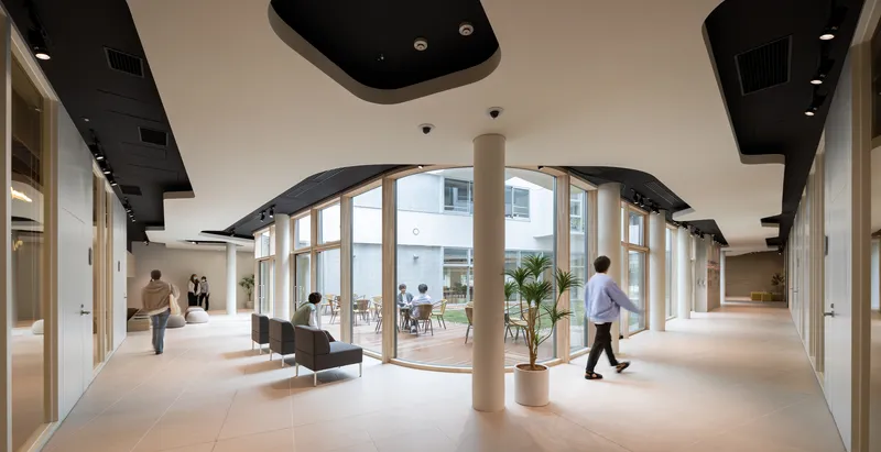 Interior corridor with curved glazed wall, black ceiling panels and cylindrical column as people walk through