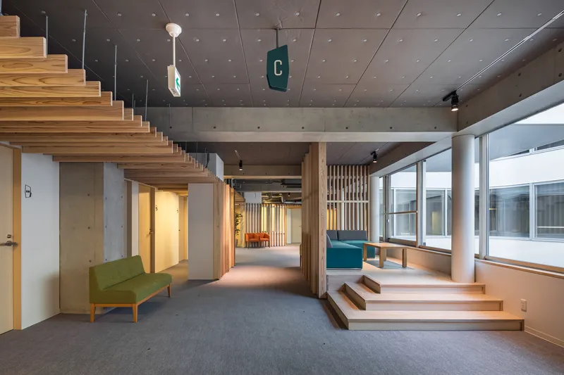 Interior view showing tiered timber steps beneath a concrete ceiling with vertical slat partitions and pendant lights