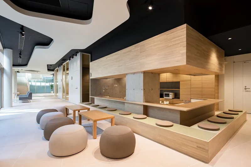 Communal kitchen and lounge with timber-clad volume overhead, floor cushions and low seating beneath sculptural black ceiling