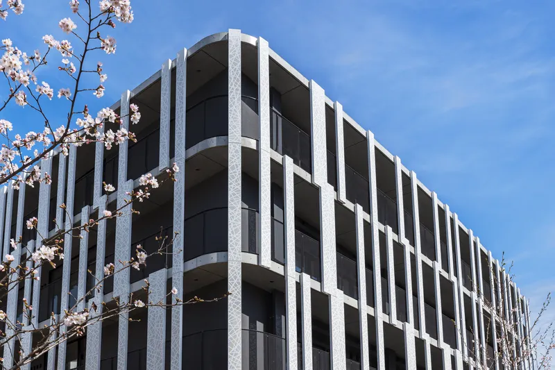 Corner facade with precast concrete frame and recessed glazing panels framed by spring blossoms