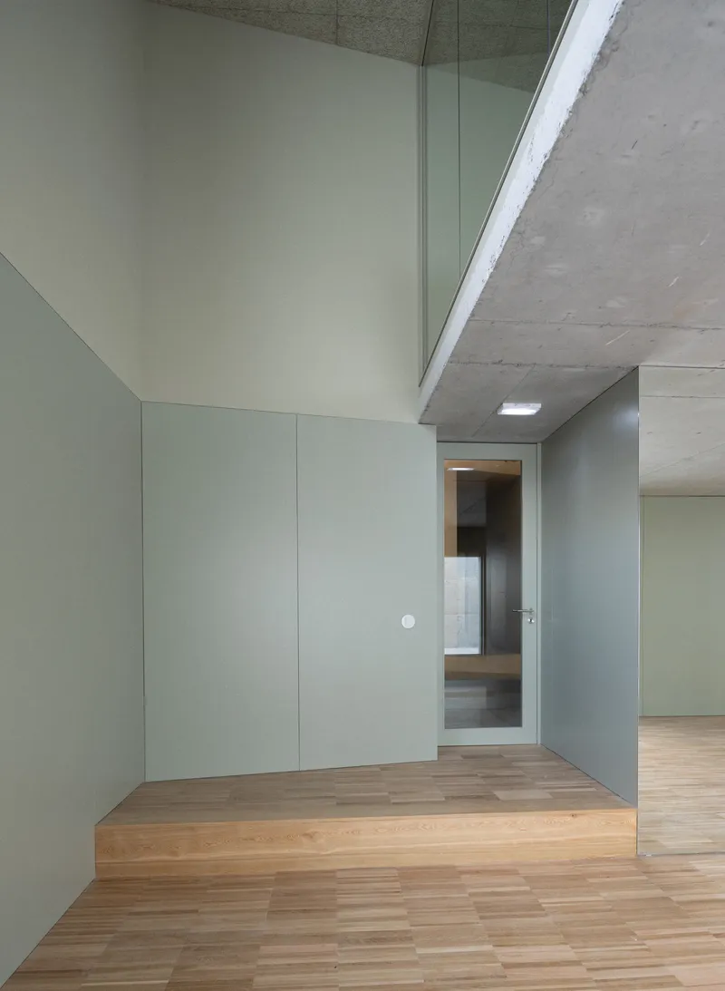 Interior corner with pale grey panels and wood flooring under a skylit concrete soffit