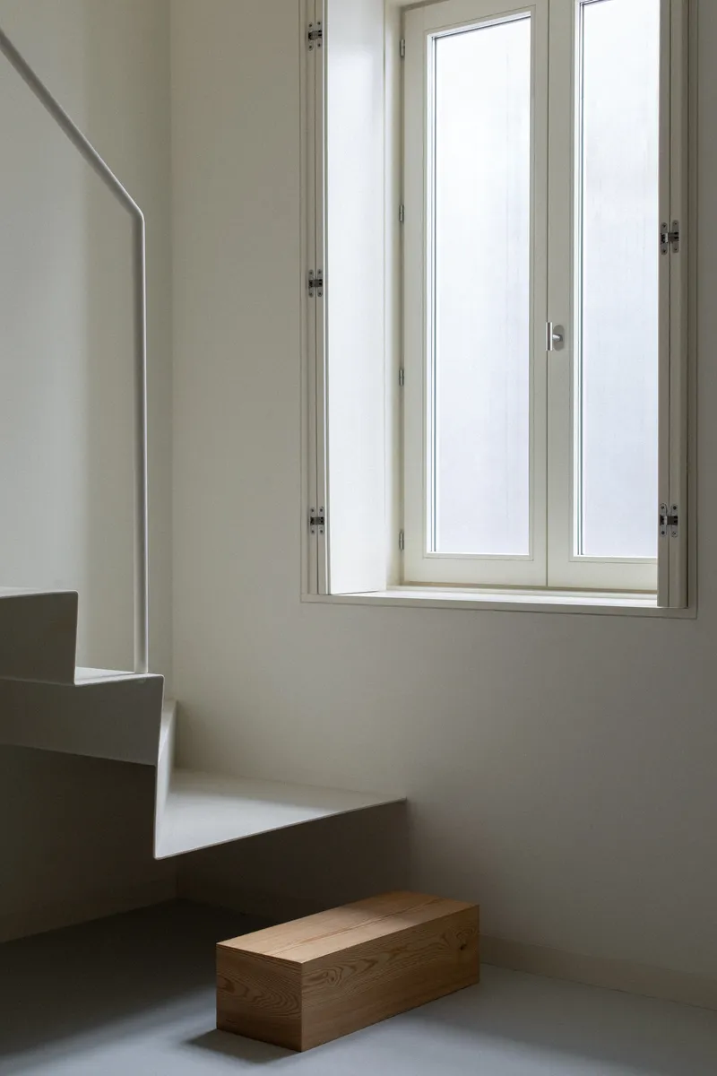 White concrete staircase with integrated handrail beside a tall casement window and timber bench