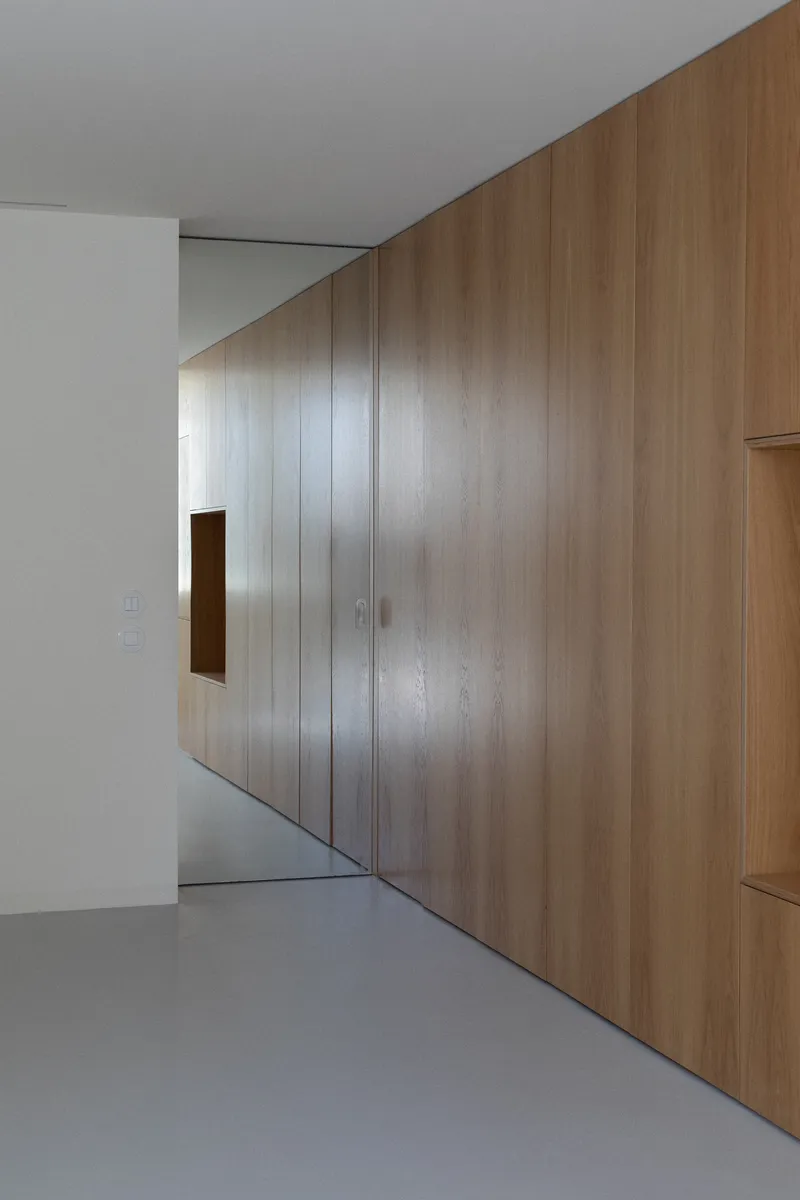 Angled oak veneer wall with small square opening above grey resin floor