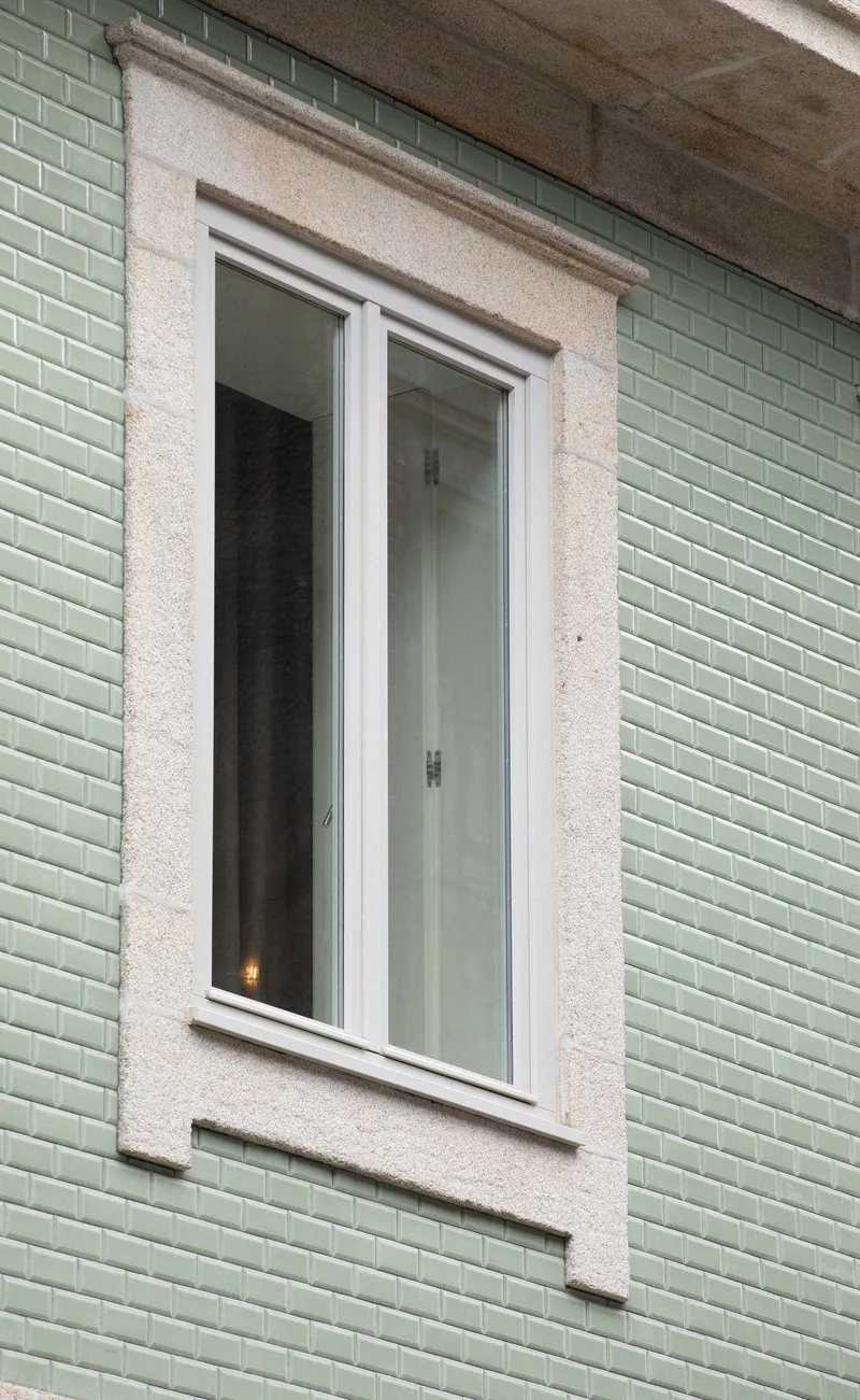 Detail of a white casement window framed in terrazzo surround against pale green glazed tile cladding