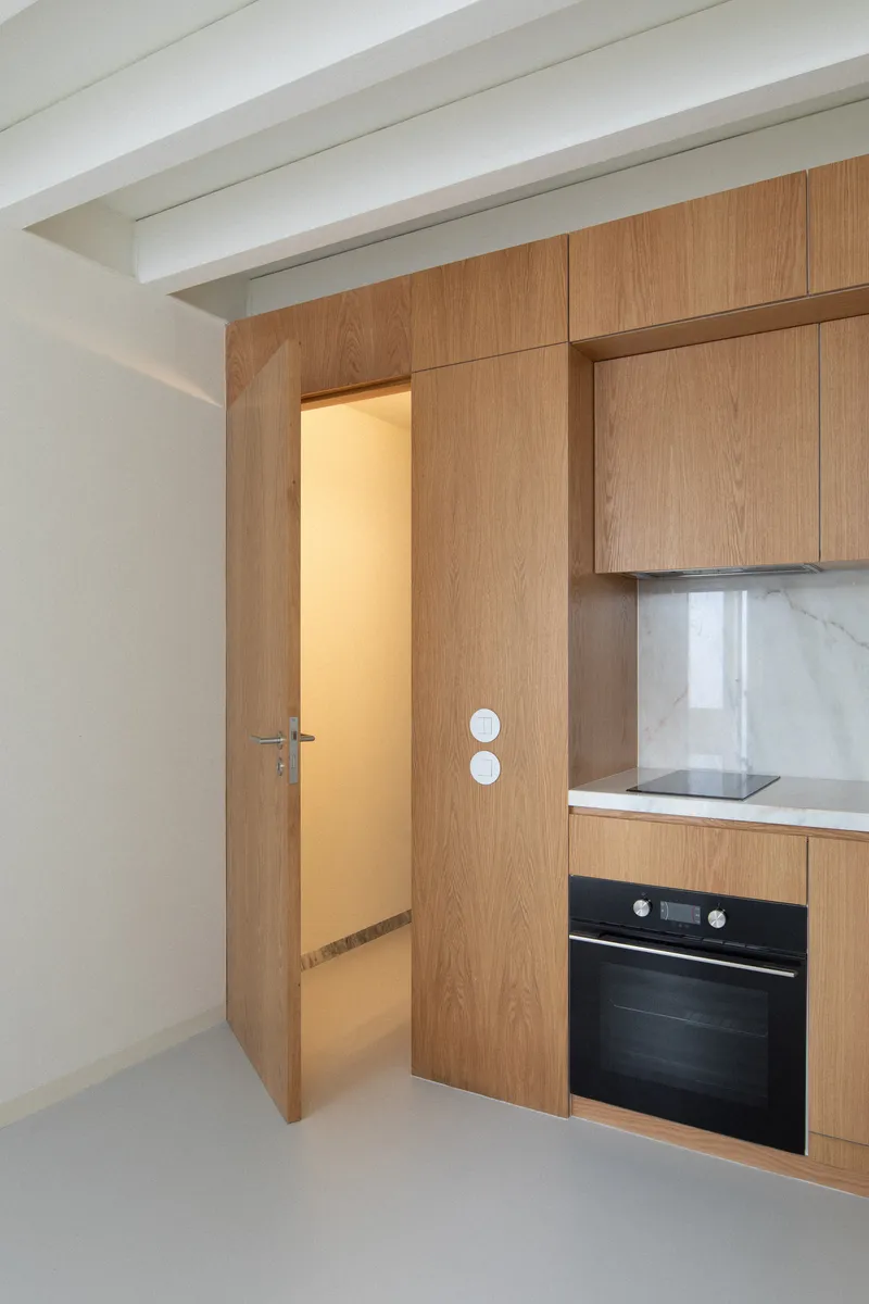 Oak veneer kitchen cabinetry with marble backsplash and open doorway beneath exposed white beams