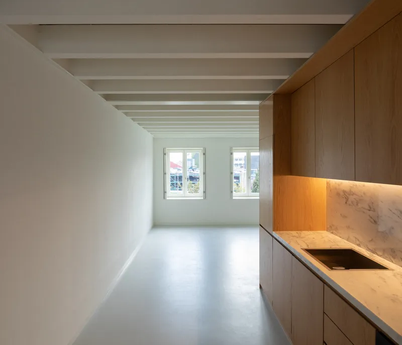 Kitchen with timber cabinetry and marble counter under an exposed beam ceiling with grey resin floor