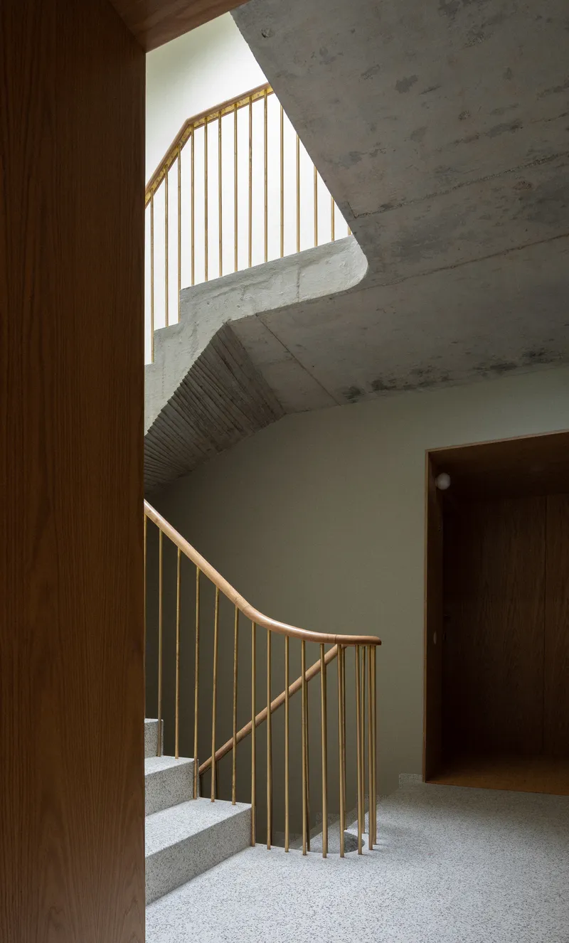 Timber-railed staircase with terrazzo treads framed by exposed concrete ceiling and wood-paneled walls