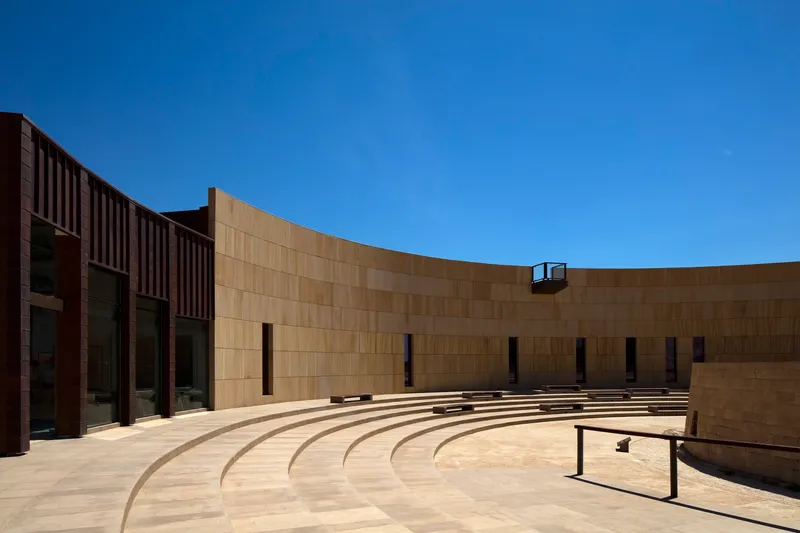 Curved outdoor amphitheater with concentric stone seating tiers under a clear blue sky