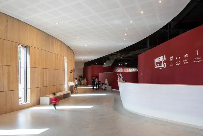 Reception lobby with curved timber wall, white coffered ceiling, and visitors at seating area