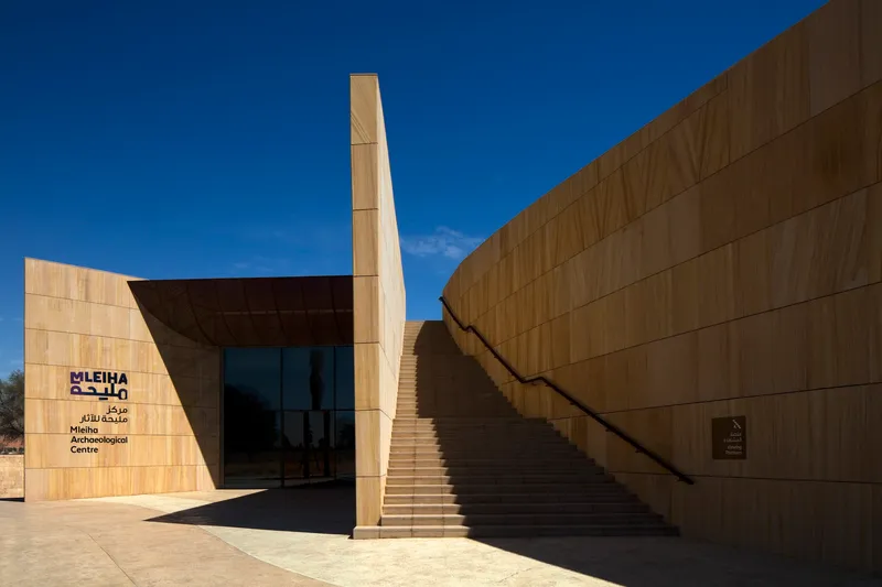 Entrance plaza showing sandstone-clad facade, freestanding tower element, and exterior staircase to roof