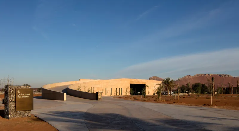 Low sandstone volume set in desert landscape with distant rocky hills and palm trees