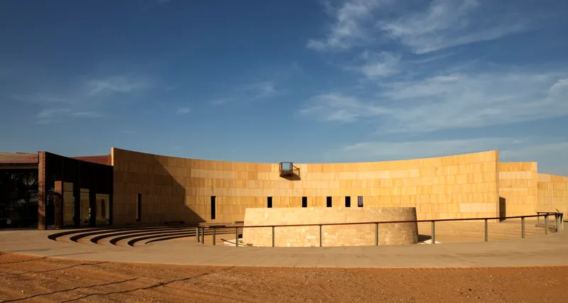 Curved sandstone facade with narrow vertical windows and stepped amphitheater seating under a blue sky