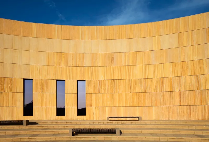 Close view of the curved sandstone facade with three tall narrow windows and stepped terrace below