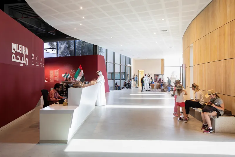 Reception hall with white desk, curved wood wall, and visitors seated on benches in daylight