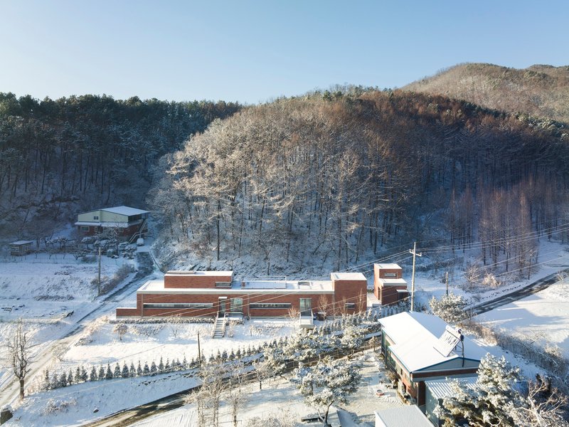 Aerial view of the horizontal brick volumes set into a snowy hillside with frosted trees behind