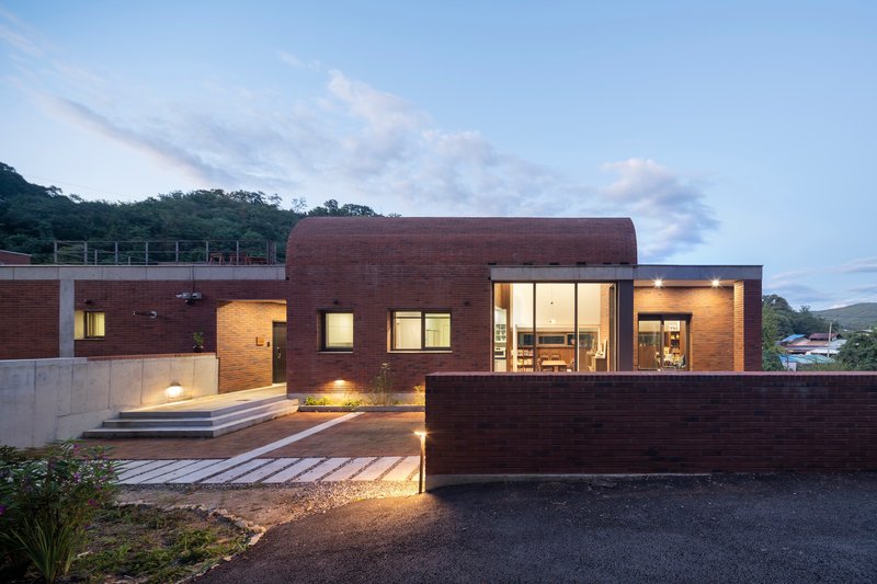 Dark brick facade with illuminated glazing and timber walkway at dusk