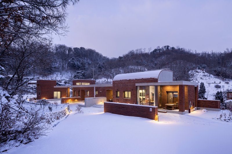Brick residence with barrel vaulted roof set in a snow-covered hillside landscape at dusk