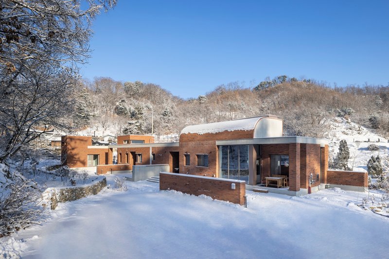 Horizontal brick volumes with curved roof element nestled in a winter valley beneath clear blue sky
