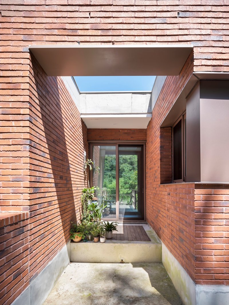 Brick-lined entry court with skylight overhead and potted plants along the concrete base