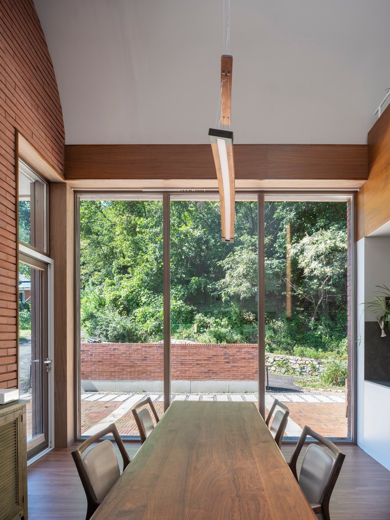 Dining room with timber pendant light and glazed wall overlooking the brick-walled garden terrace