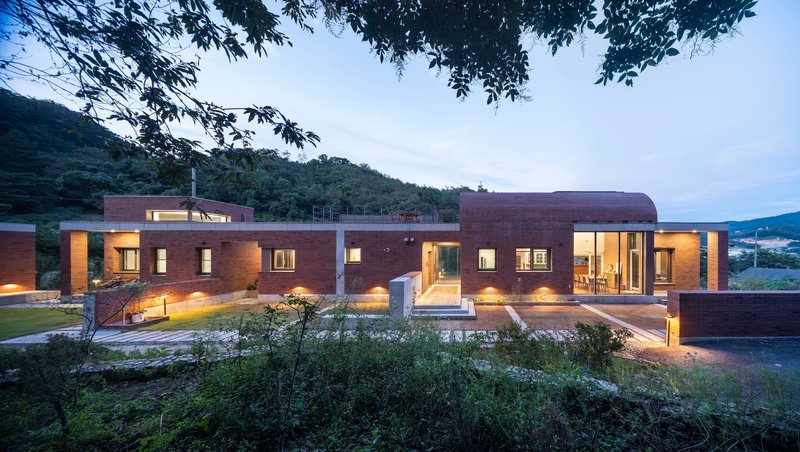 Evening view of the brick facade with illuminated windows and landscaped foreground planting beds