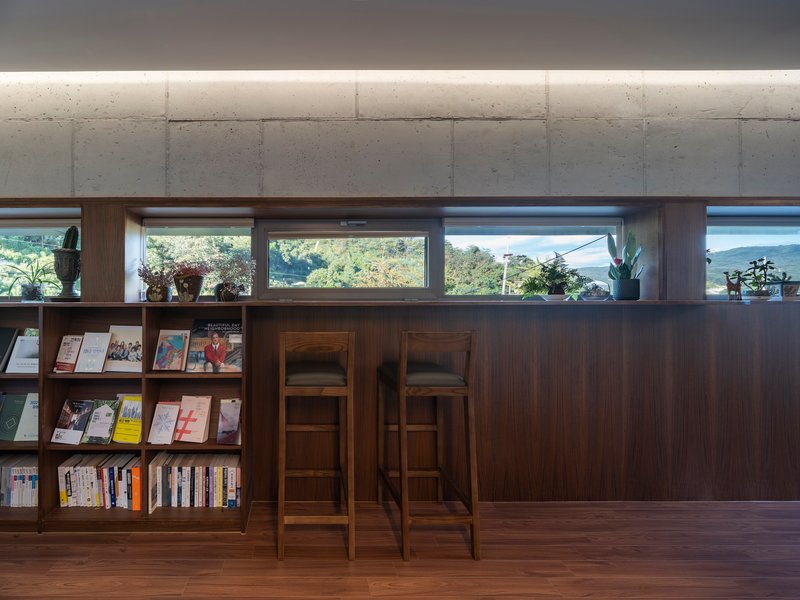 Interior counter with timber bookshelves and stools below a band of clerestory windows admitting daylight