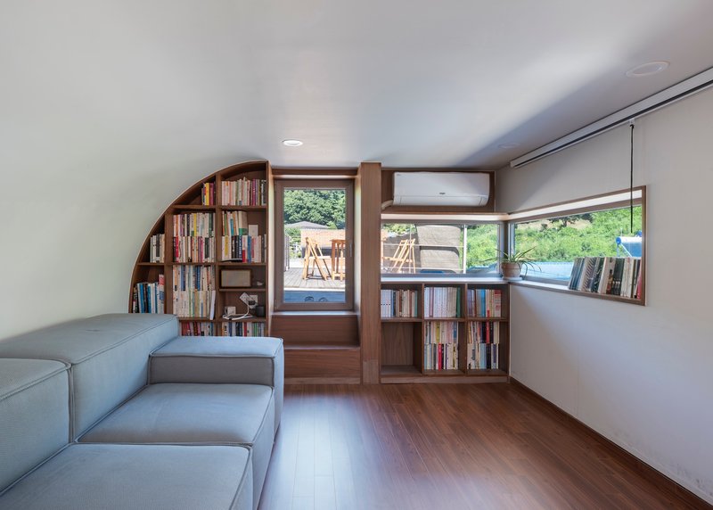 Reading room with curved timber bookshelves and corner windows overlooking the surrounding greenery