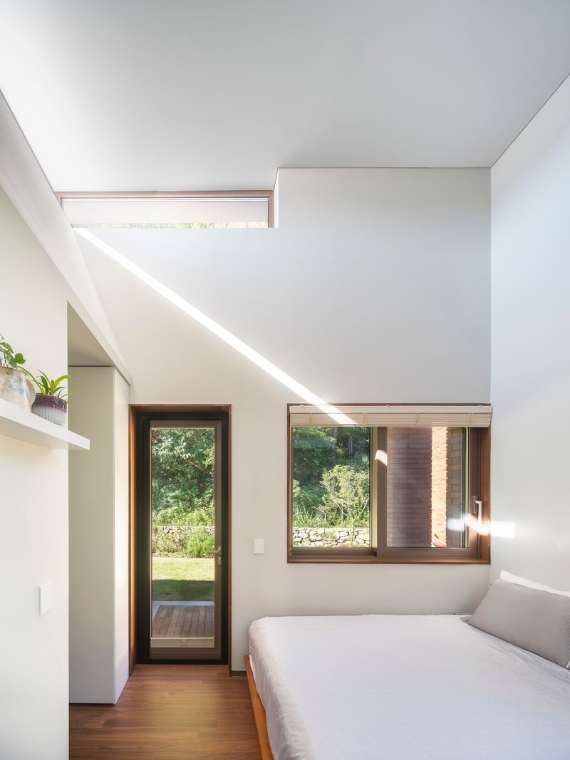 Bedroom with high clerestory window and corner glazing bringing afternoon light into the white interior