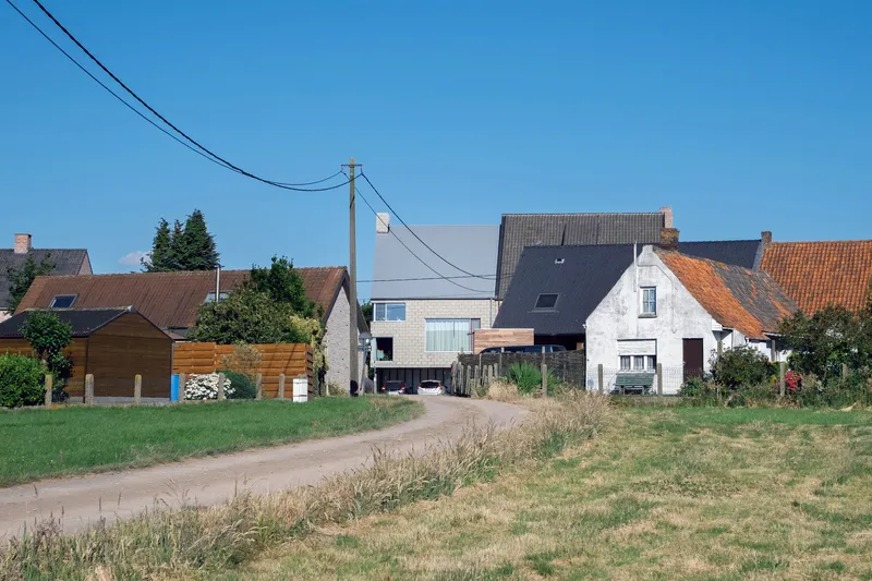 Street view showing the pale brick volume inserted between traditional pitched-roof houses under a clear sky