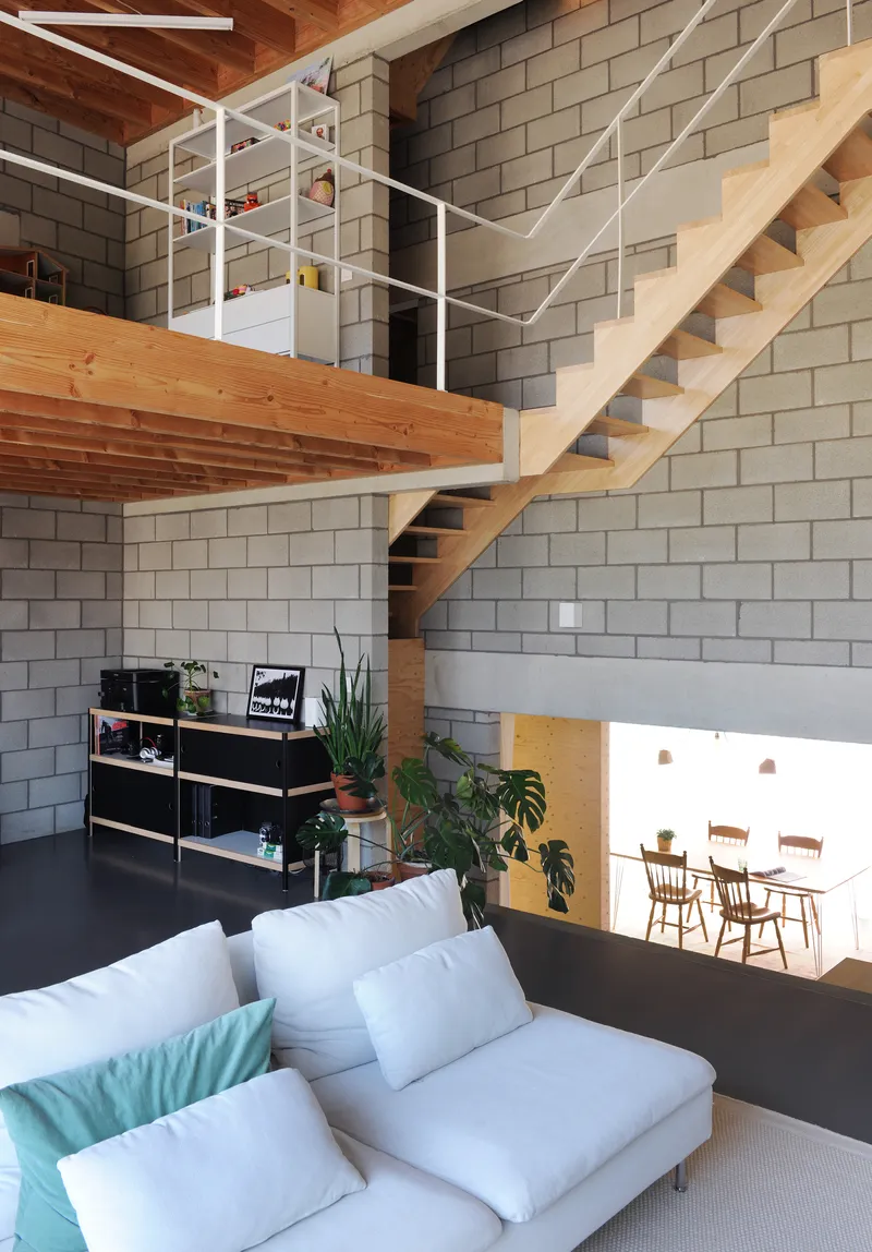 Double-height living space with timber stair ascending to mezzanine past concrete block wall