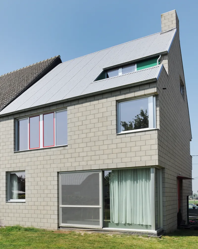 Side facade displaying pale masonry walls, corrugated roof slope, and stacked window openings with green accents