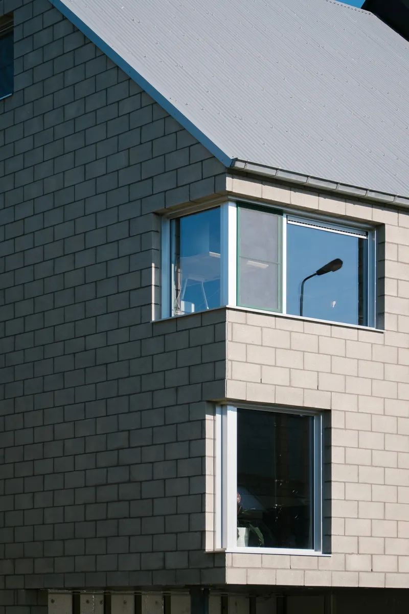 Exterior corner detail with dark green tile cladding meeting cream panels under a corrugated metal roof